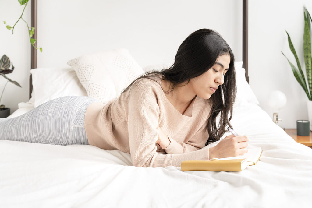 Dark-haired woman journaling in bed
